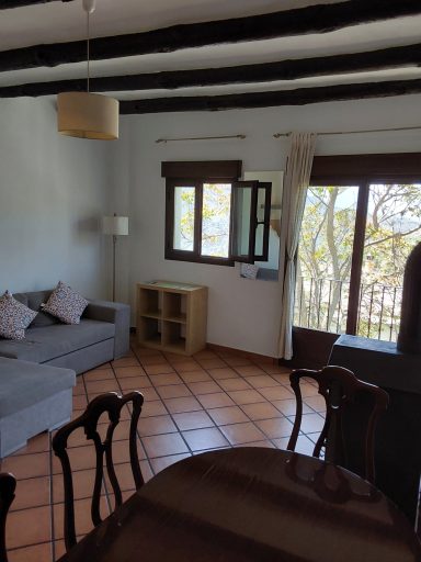 Sala de estar luminosa con sofá, mesa de comedor y ventanas hacia un paisaje natural.